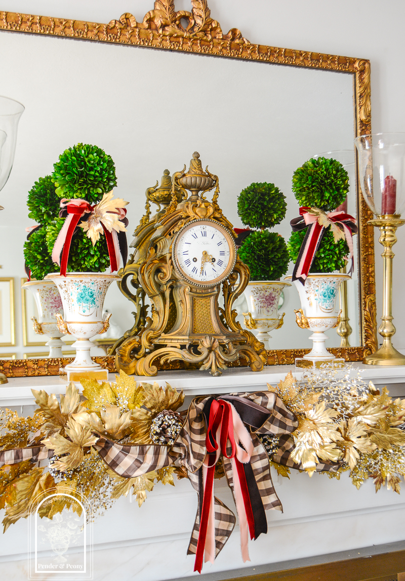 A gold maple leaf garland for fall mantel decor decorated with brown, pink, and burgundy ribbons