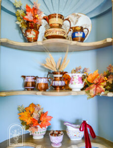 Lustre ware jugs arranged on corner shelf with autumn leaves, wheat, and acorns