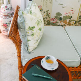 Wicker daybed with chintz pillow and side table with china teacup and green leather note book - cultivate beauty in your home with just a few small efforts