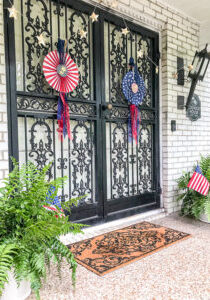 July 4th decorated front door with red, white, and blue DIY patriotic rosettes and star twinkle lights.
