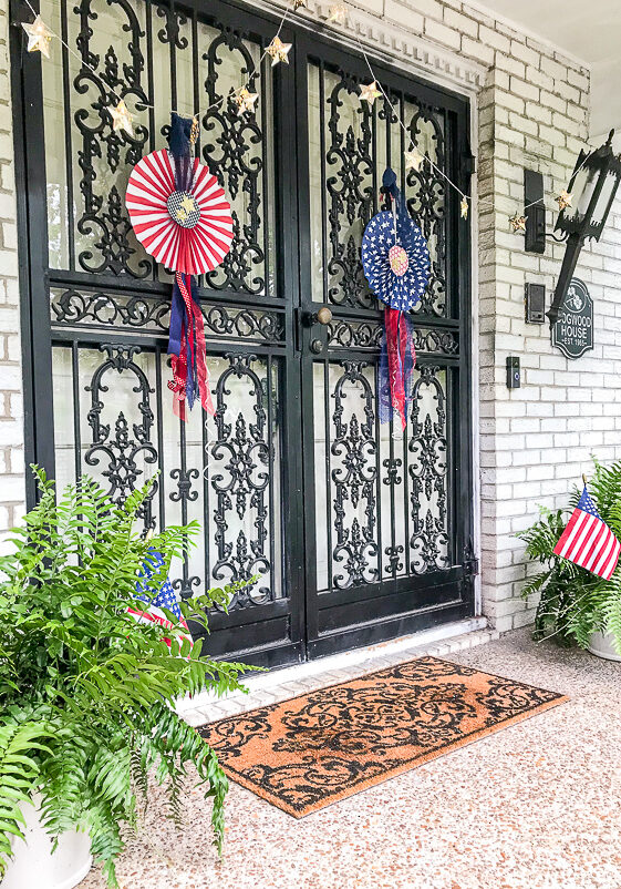 July 4th decorated front door with red, white, and blue DIY patriotic rosettes and star twinkle lights.