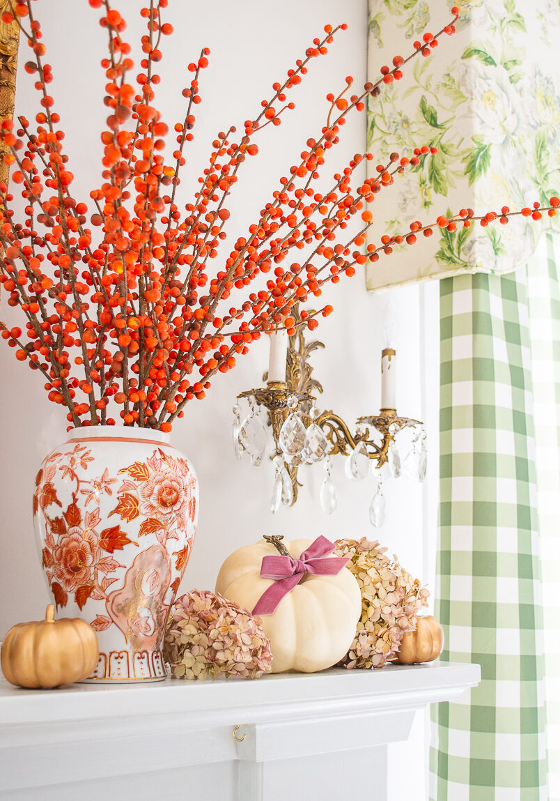 Small white pumpkin nestled in dried hydrangea blooms surrounding an orange and white Chinese vase filled with orange berry branches