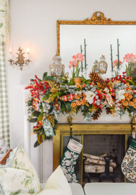 A Grand Botanical Christmas mantel decoration with DIY garland made of magnolia, pine, cedar, red berries, gold fern, orange slices, ribbon, and amaryllis.