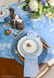 An Easter table in blue and white with Wedgwood Queen's Ware, chocolate bunnies, French wire basket filled with flowers, and April Cornell chintz tablecloth.
