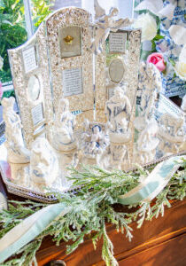 Blue and white Nativity set on silver tray with cedar garland surrounding and silver framed Bible verses in background - top view of Baby Jesus