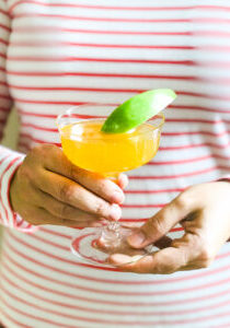 A bubbly apple cocktail in champagne coupe with green apple slice held in front of striped shirt
