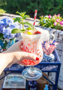 Cherry mint lemonade cocktail in white splatterware glass with paper straw and mint sprig