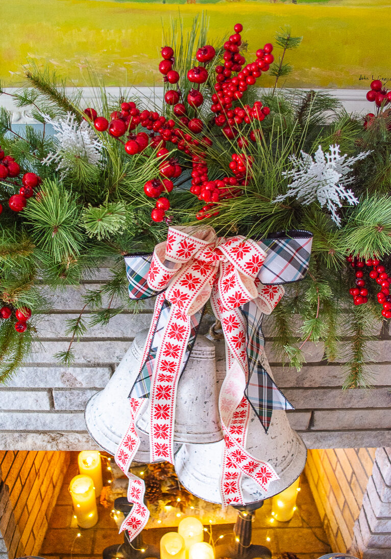 detail of snowflake ribbon bow and white bells hanging from faux pine swag on mantel