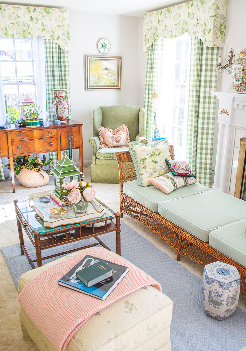 My grandmillennial living room decorated in green, white, blue, and pink with chintz and gingham window treatments, wicker furniture, and colorful accessories.