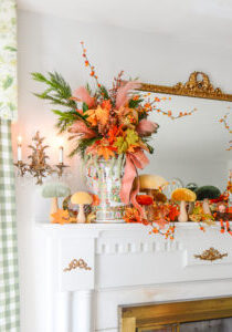 A magical autumn mantel arrangement with velvet mushrooms, Rose Medallion, fall leaves, bittersweet, and whimsical elves