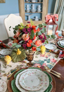 Autumn table decor with pretty floral chintz, plaid napkins, maple leaf china, and pumpkin floral centerpiece