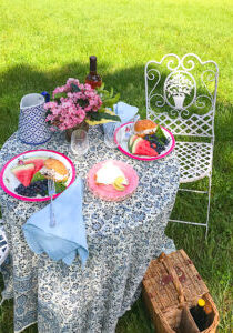Picnic table set with vintage dishes, cloth napkins, and silver. Plates filled with chicken salad and fruit.