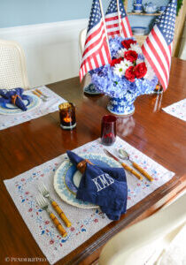 A red, white, and blue floral tablescape for Independence Day. Set with Sarah Flint placemats, Wedgwood Queen's Ware, Mottahedeh blue lace, bamboo flatware, hydrangea, and flags.
